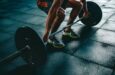 Person i knäböjsgrepp lyfter en skivstång med viktskivor på gymgolv